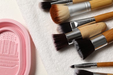 Photo of Clean makeup brushes with towel and cleansing pad on white table, flat lay