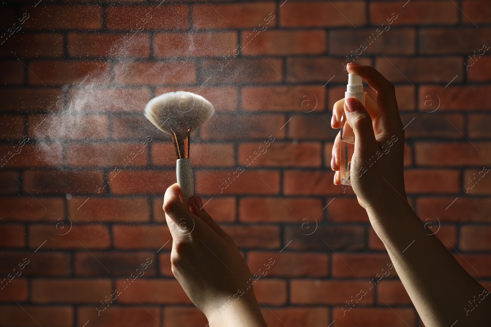 Photo of Woman cleaning makeup brushes with spray against brick wall, closeup