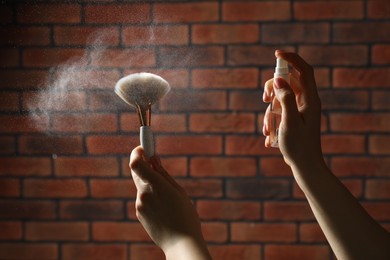 Photo of Woman cleaning makeup brushes with spray against brick wall, closeup