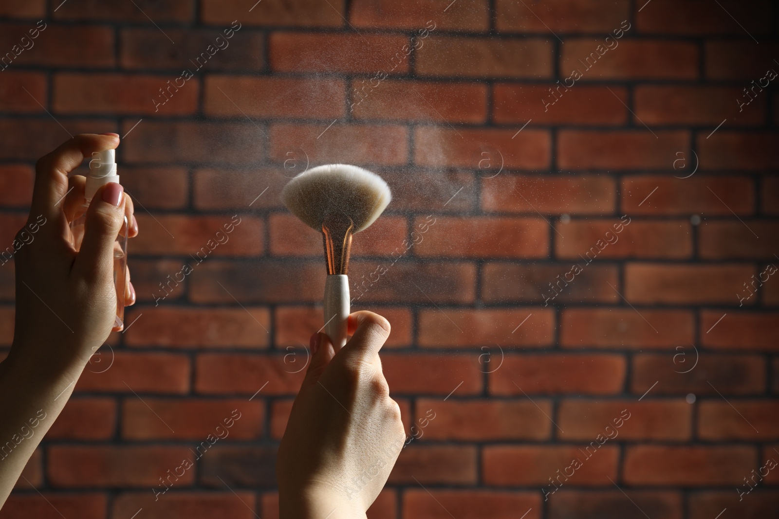 Photo of Woman cleaning makeup brushes with spray against brick wall, closeup. Space for text