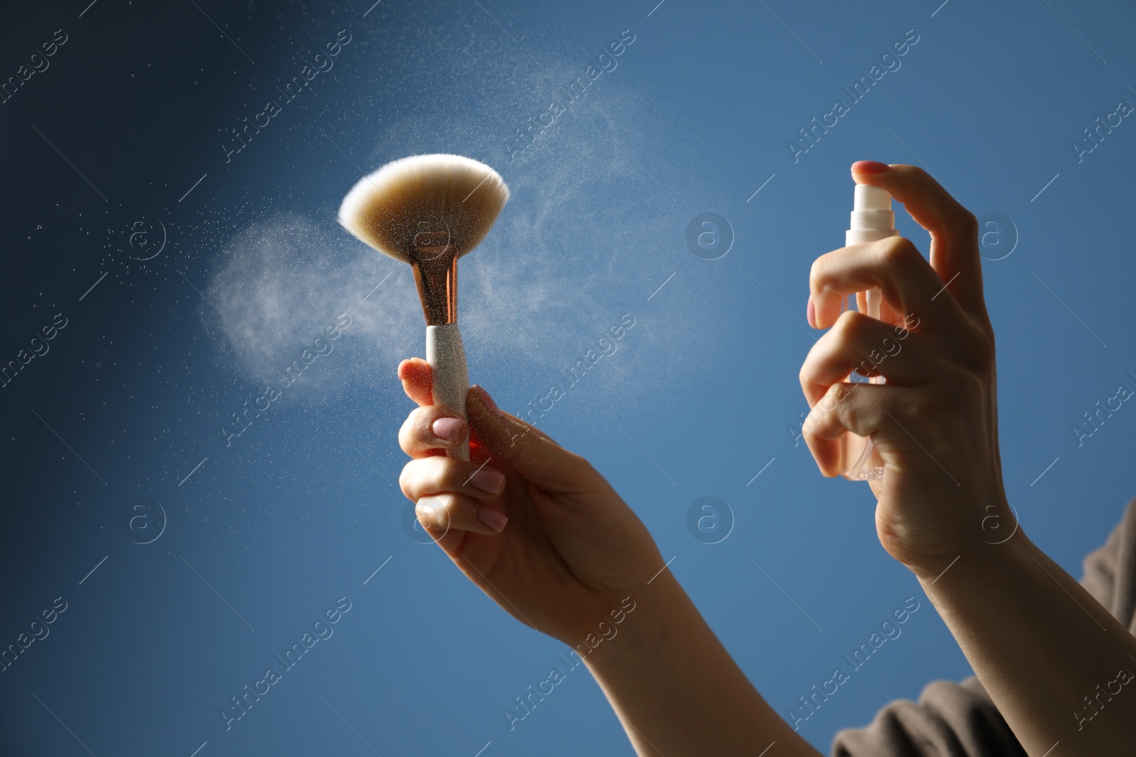 Photo of Woman cleaning makeup brush with spray on blue background, closeup