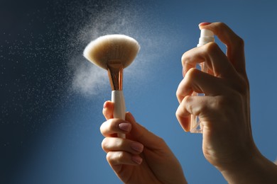 Photo of Woman cleaning makeup brush with spray on blue background, closeup