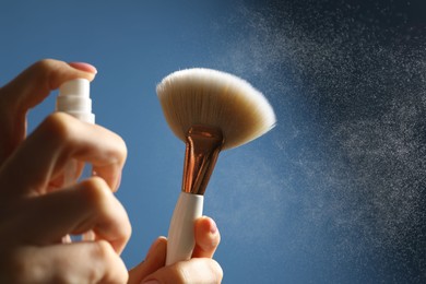 Photo of Woman cleaning makeup brush with spray on blue background, closeup