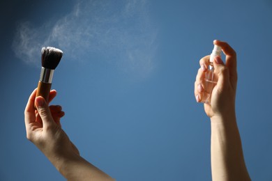 Photo of Woman cleaning makeup brush with spray on blue background, closeup