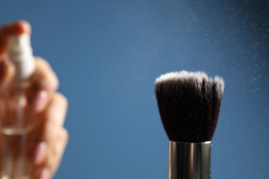 Photo of Woman cleaning makeup brush with spray on blue background, selective focus