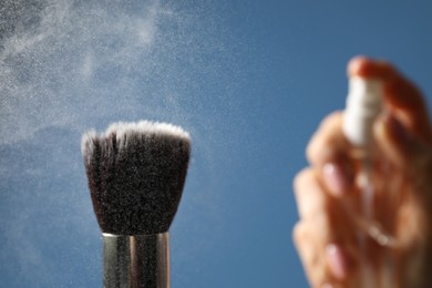 Photo of Woman cleaning makeup brush with spray on blue background, selective focus