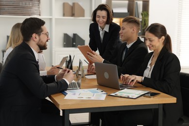 Photo of Coworkers with different devices working together at wooden table in office