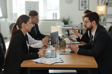 Photo of Coworkers with different devices working together at wooden table in office