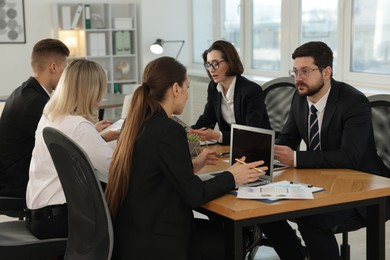 Photo of Coworkers with different devices working together at wooden table in office