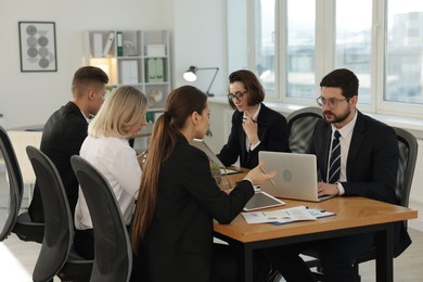 Photo of Coworkers with different devices working together at wooden table in office