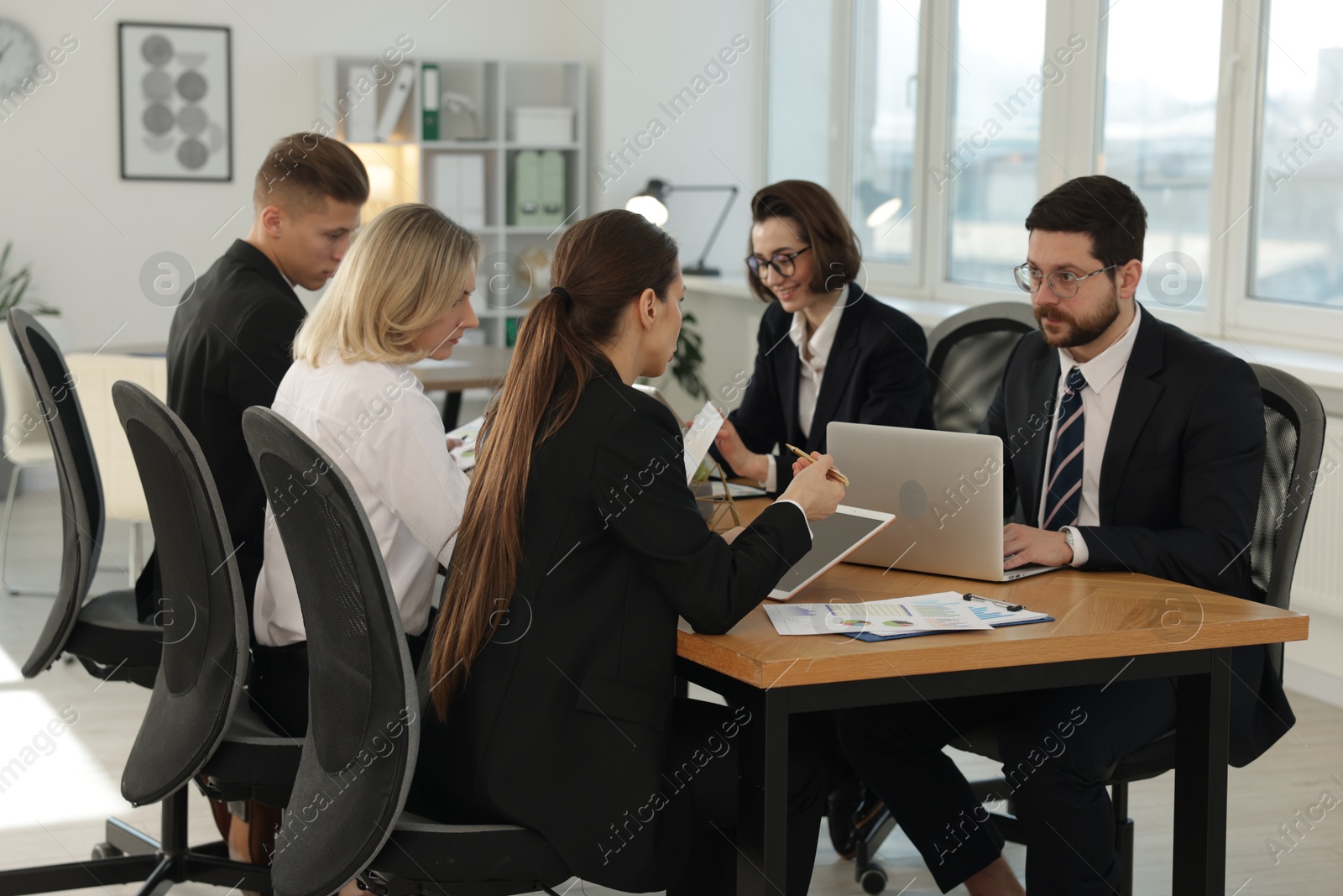 Photo of Coworkers with different devices working together at wooden table in office