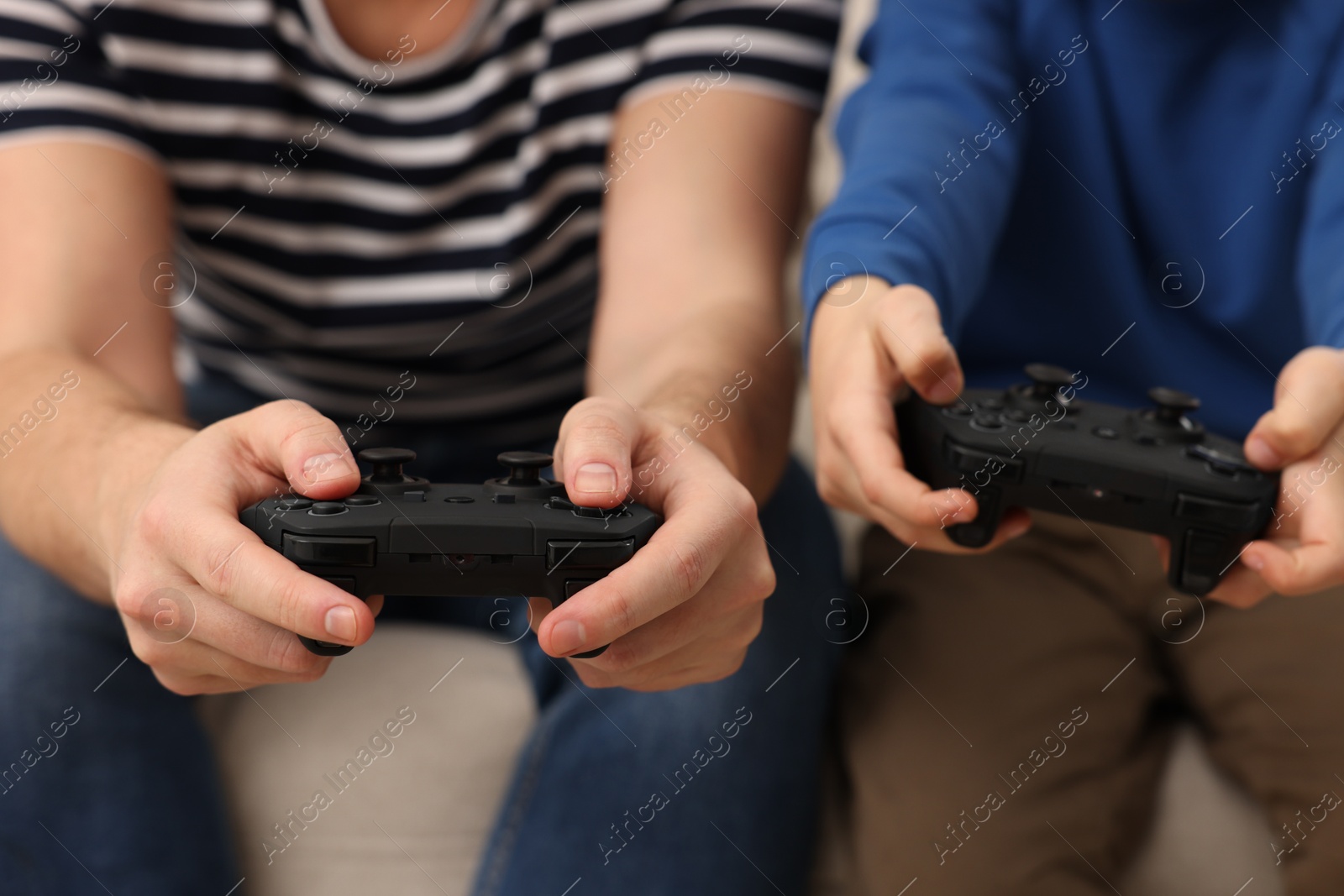 Photo of Father and his son playing video games on sofa indoors, closeup