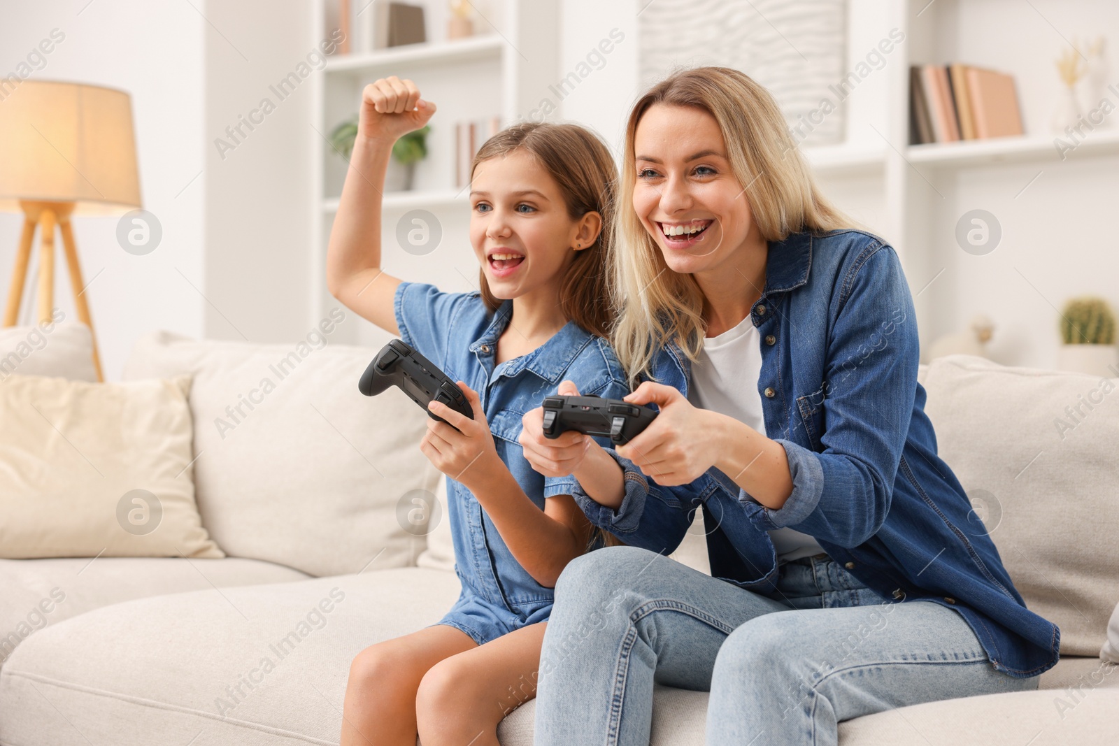 Photo of Happy mother and her daughter playing video games on sofa in living room