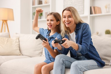 Photo of Happy mother and her daughter playing video games on sofa in living room