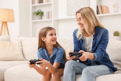 Photo of Happy mother and her daughter playing video games on sofa in living room