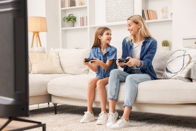 Photo of Happy mother and her daughter playing video games on sofa in living room