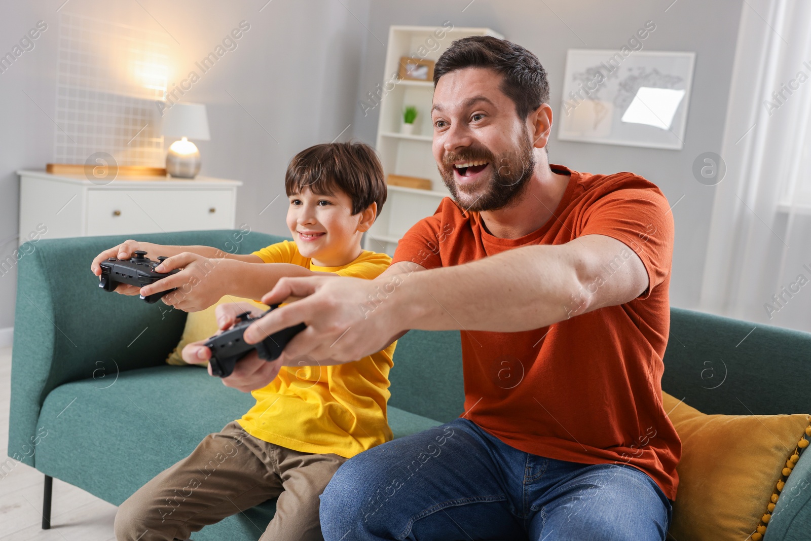 Photo of Happy father and his son playing video games on sofa in living room