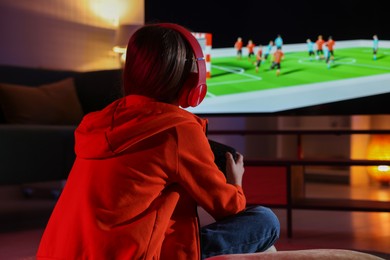 Photo of Little girl in headphones playing video game at home, back view