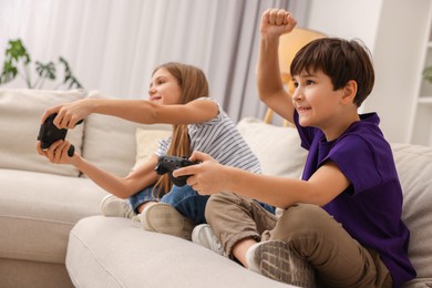 Photo of Cute kids playing video games on sofa in living room