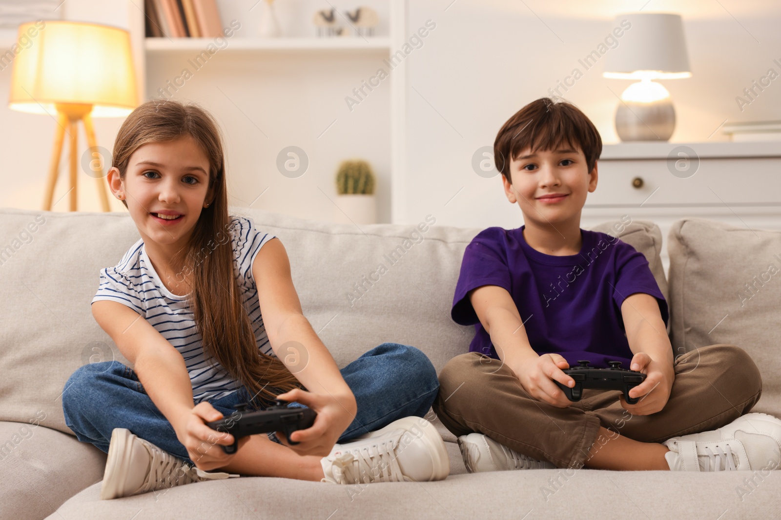 Photo of Cute kids playing video games on sofa in living room