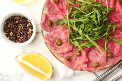 Delicious beef carpaccio served on white marble table, flat lay