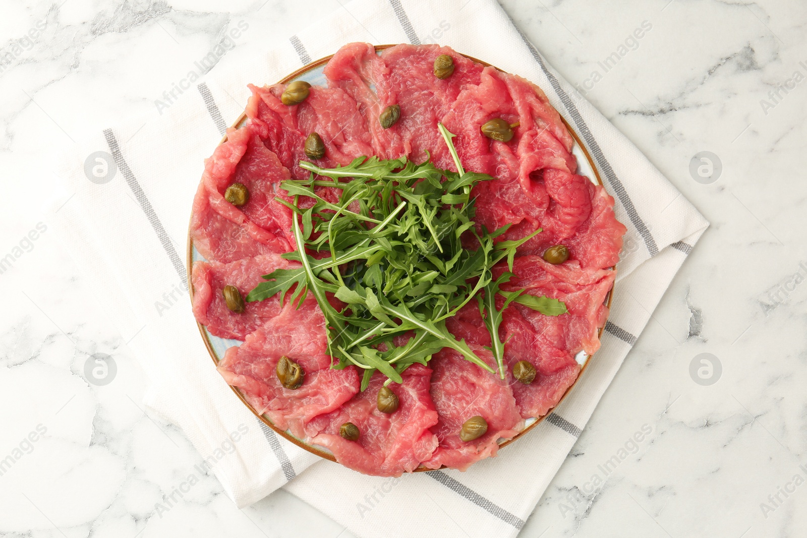 Photo of Delicious beef carpaccio with arugula and capers on white marble table, top view