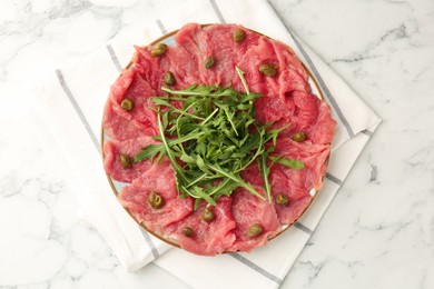 Delicious beef carpaccio with arugula and capers on white marble table, top view