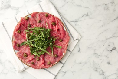 Photo of Delicious beef carpaccio with arugula and capers on white marble table, top view. Space for text