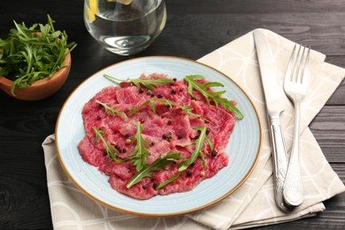 Photo of Fresh beef carpaccio with arugula and peppercorns on black wooden table