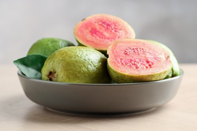 Fresh guava fruits in bowl on wooden table against blurred grey background, closeup