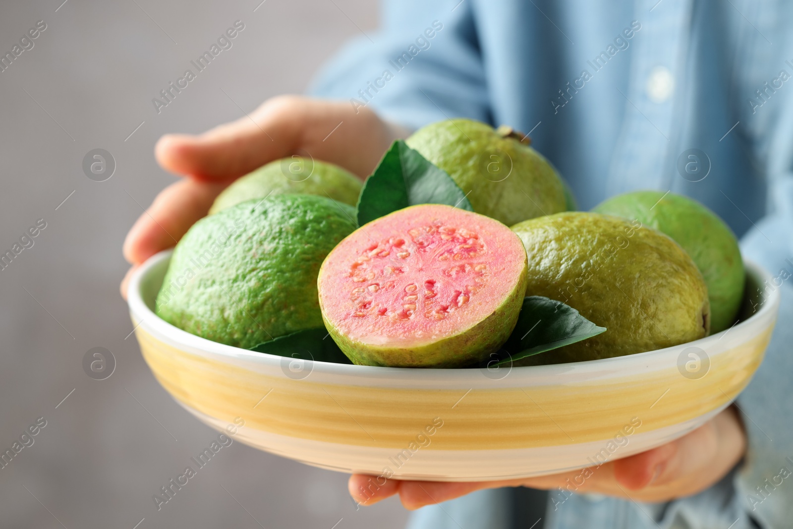 Photo of Woman with bowl of fresh guava fruits on blurred grey background, closeup