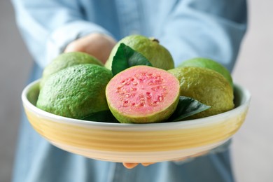 Photo of Woman with bowl of fresh guava fruits on blurred background, closeup