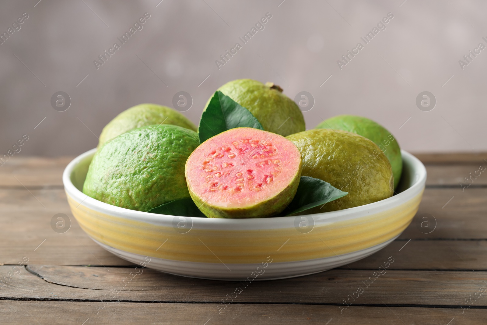 Photo of Fresh guava fruits in bowl on wooden table against blurred grey background, closeup