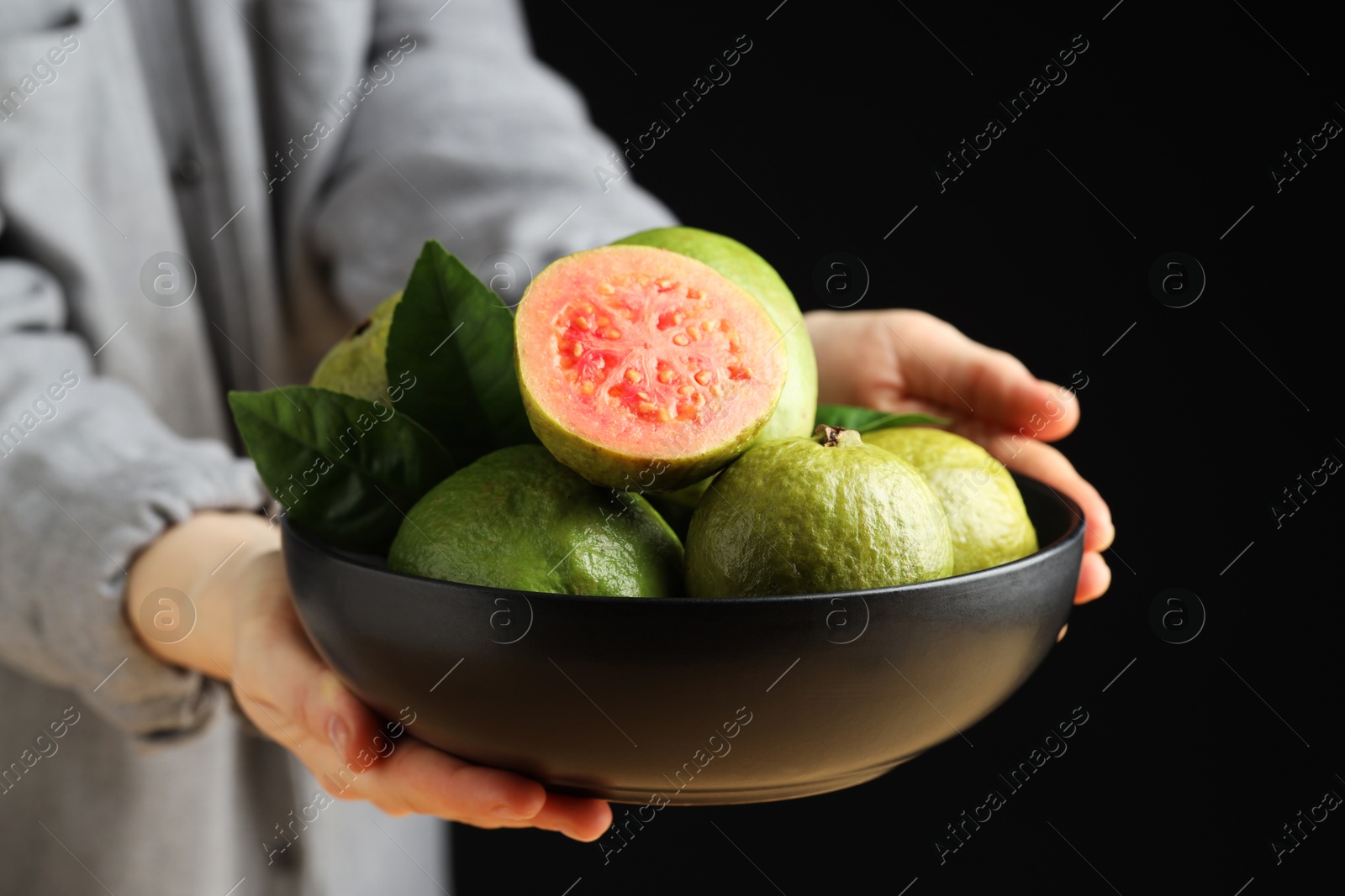 Photo of Woman with bowl of fresh guava fruits on black background, closeup