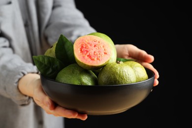 Woman with bowl of fresh guava fruits on black background, closeup