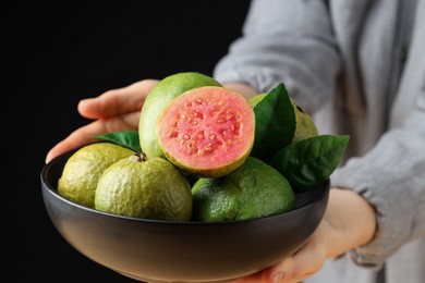 Photo of Woman with bowl of fresh guava fruits on black background, closeup