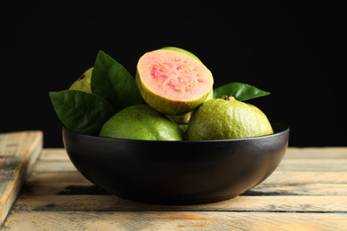 Photo of Fresh guava fruits in bowl on wooden table against black background, closeup