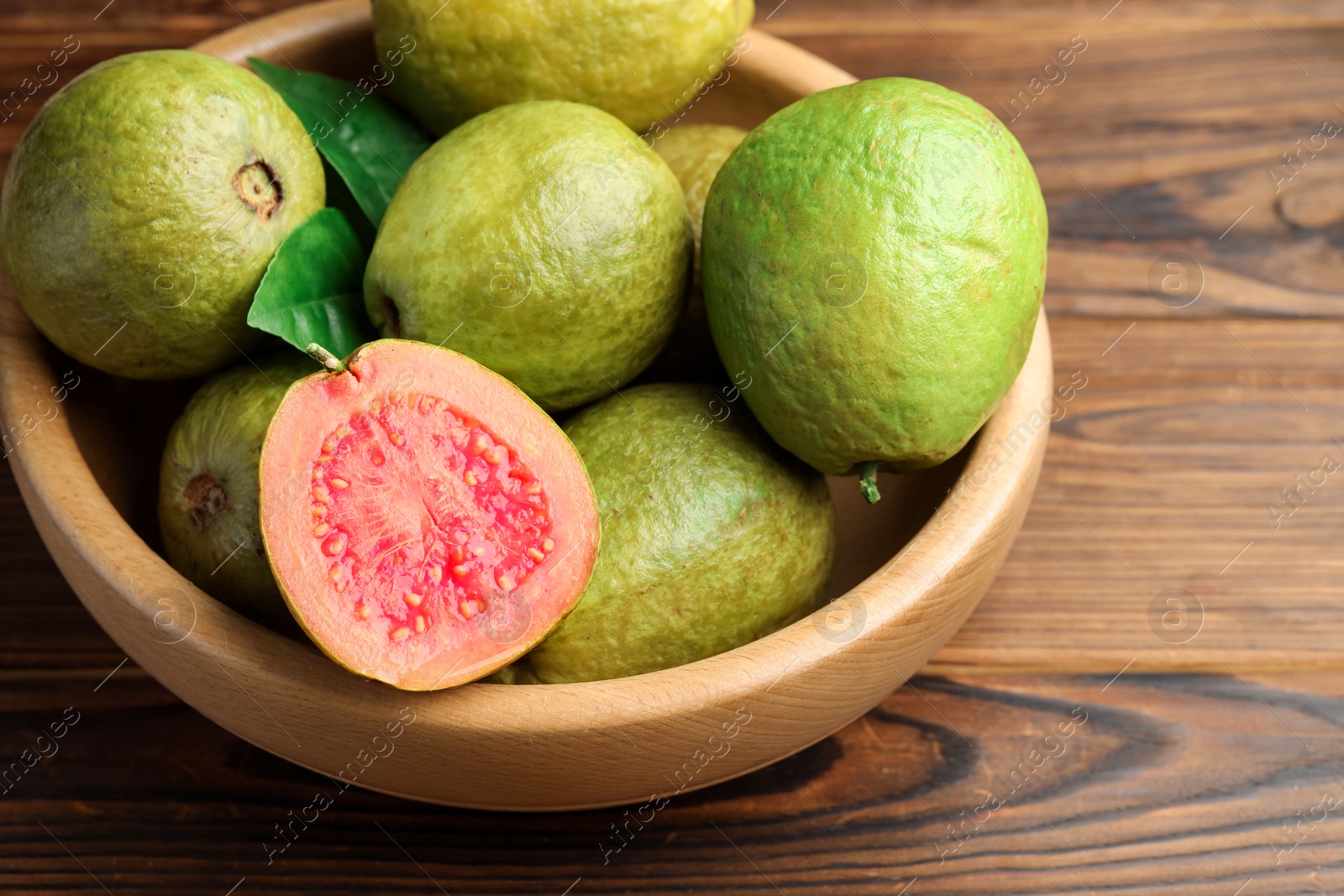 Photo of Fresh cut and whole guava fruits in bowl on wooden table, closeup