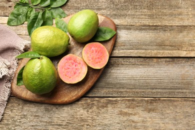 Photo of Fresh whole and cut guava fruits on wooden table, flat lay. Space for text