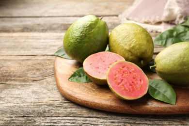 Fresh whole and cut guava fruits on wooden table, closeup. Space for text