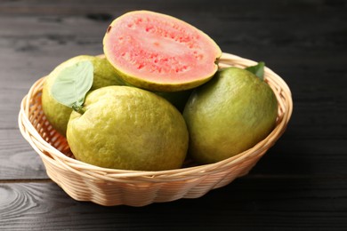 Fresh whole and cut guava fruits in wicker basket on black wooden table, closeup