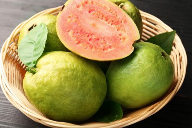 Fresh whole and cut guava fruits in wicker basket on black wooden table, closeup