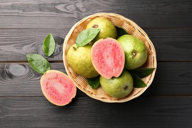 Photo of Fresh whole and cut guava fruits on black wooden table, flat lay