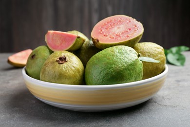 Photo of Fresh whole and cut guava fruits in bowl on grey textured table, closeup