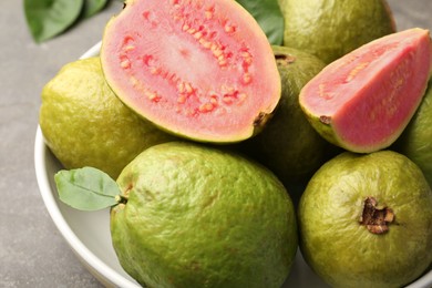 Fresh whole and cut guava fruits in bowl on grey table, closeup