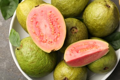 Photo of Fresh whole and cut guava fruits in bowl on grey table, top view