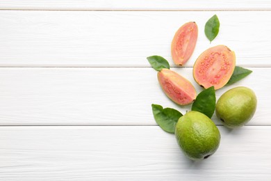 Photo of Fresh whole and cut guava fruits on white wooden table, flat lay. Space for text