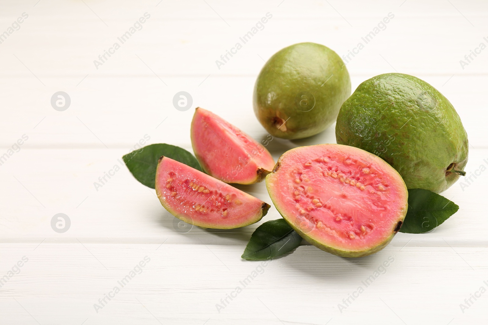 Photo of Fresh whole and cut guava fruits on white wooden table. Space for text