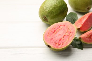 Photo of Fresh whole and cut guava fruits on white wooden table, closeup. Space for text