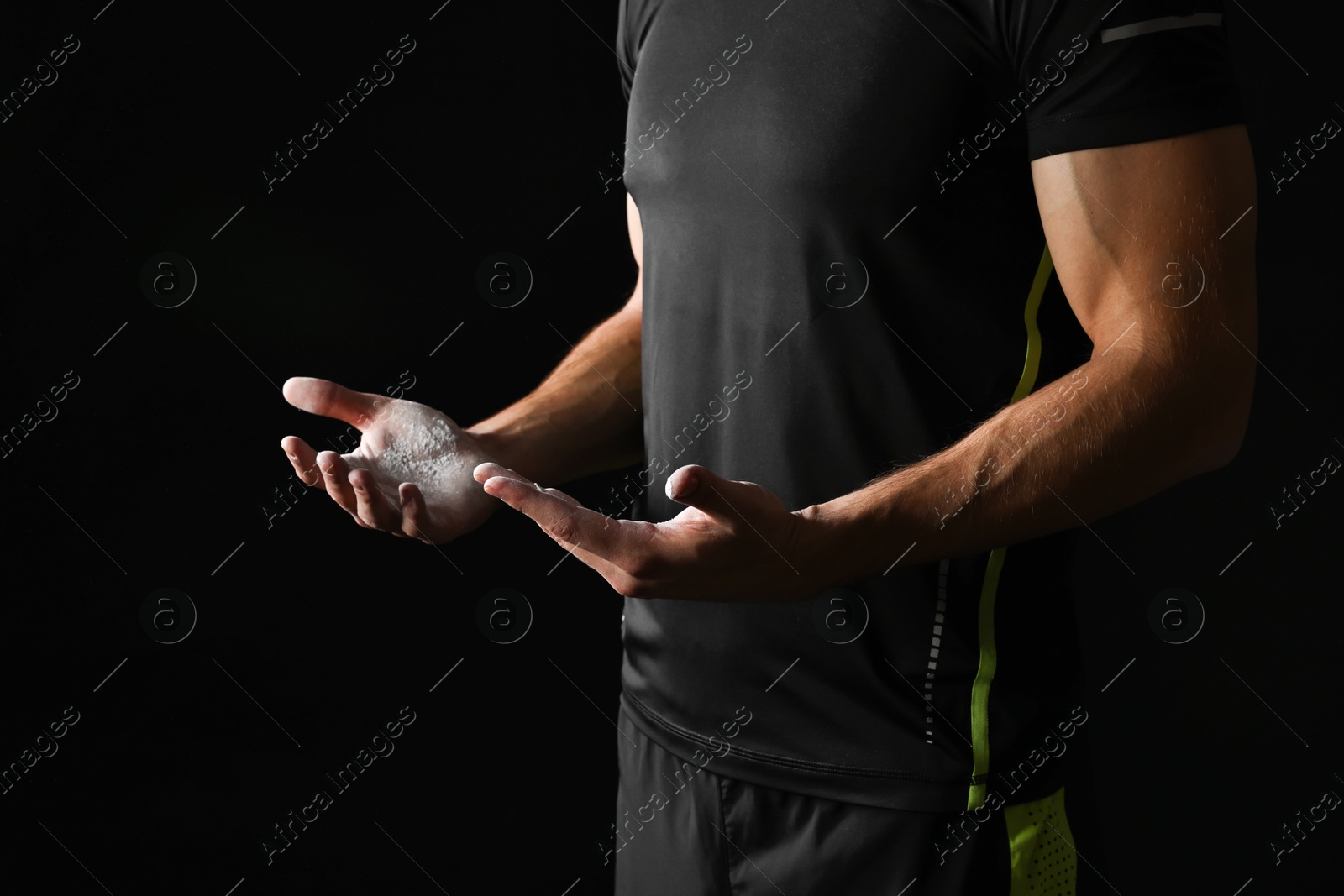 Photo of Man with talcum powder on hands before training against black background, closeup